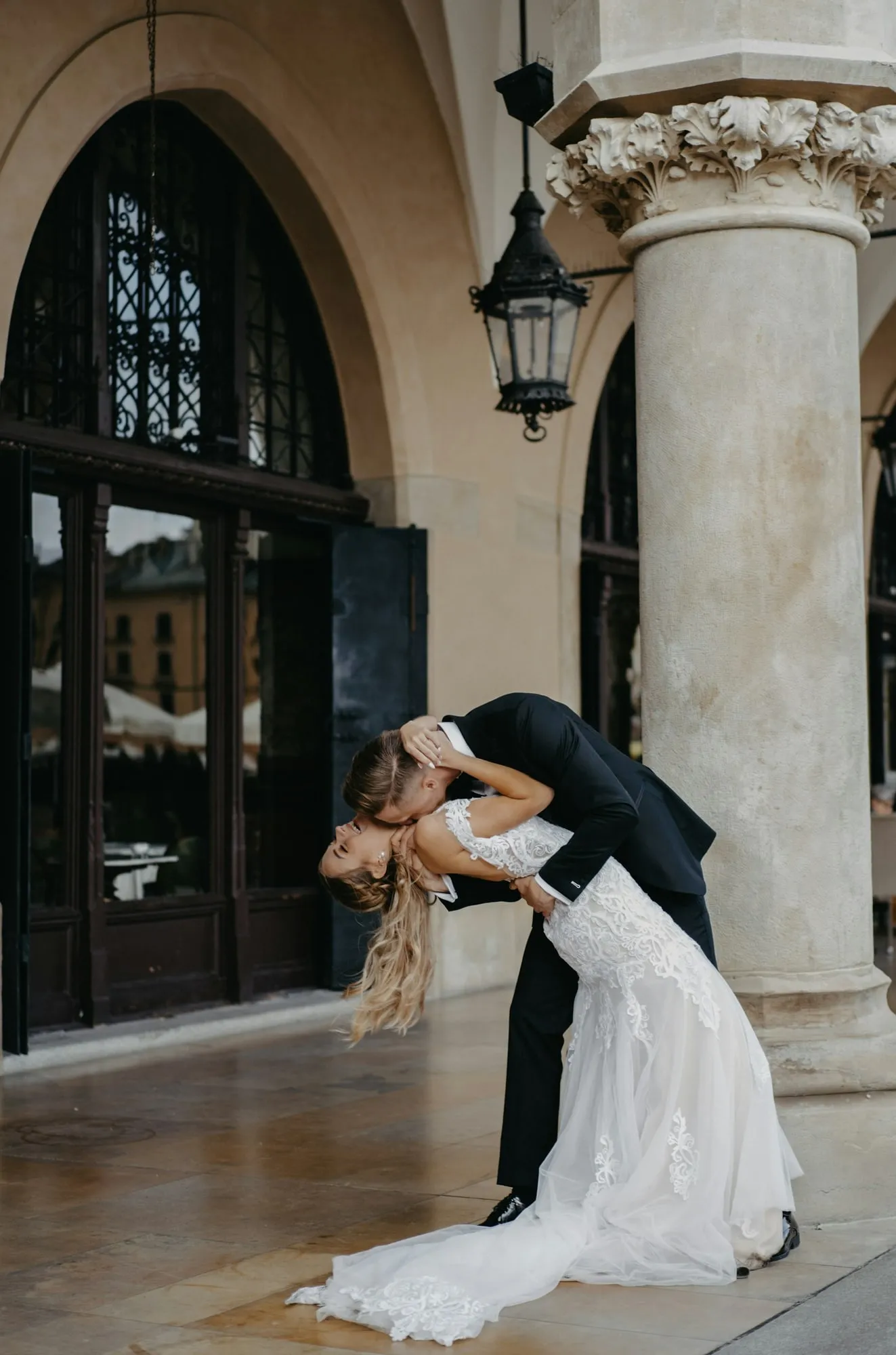 The groom dips the bride beneath palace arcades