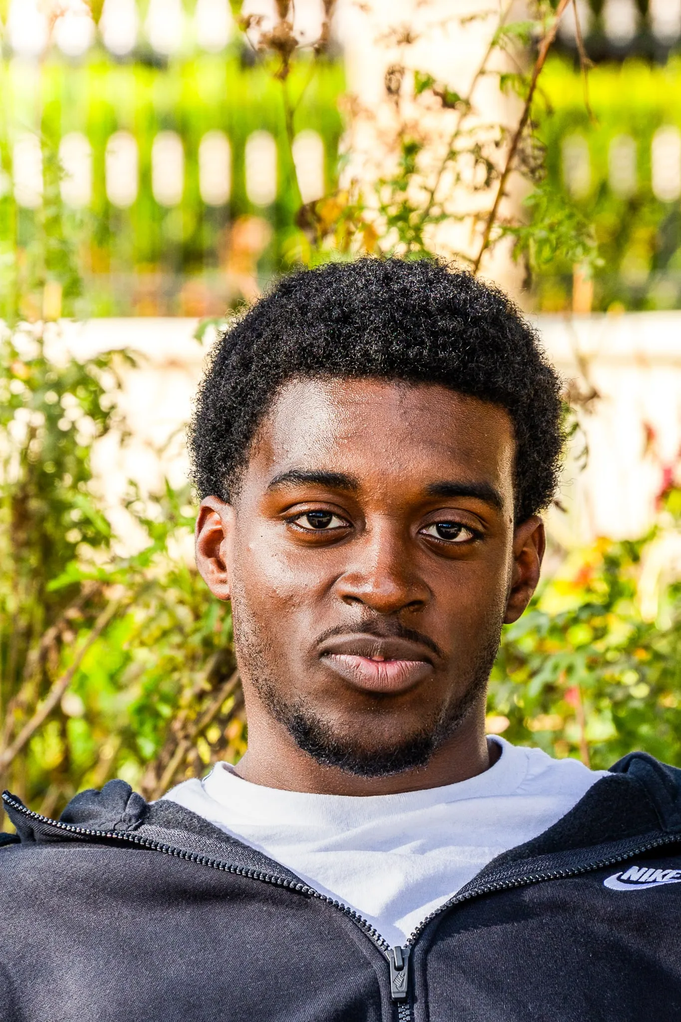 Close portrait of a young man in natural light, greenery behind