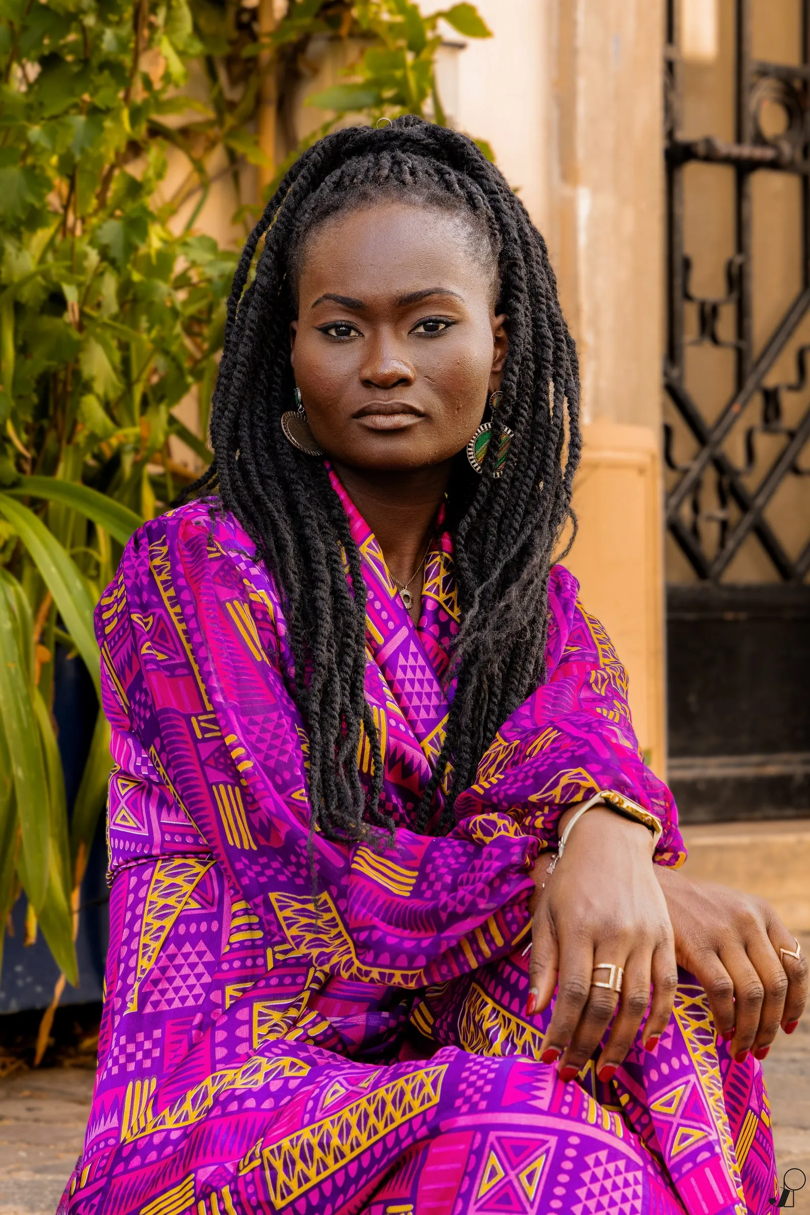 Woman with long braids in a magenta wax outfit, looking straight ahead